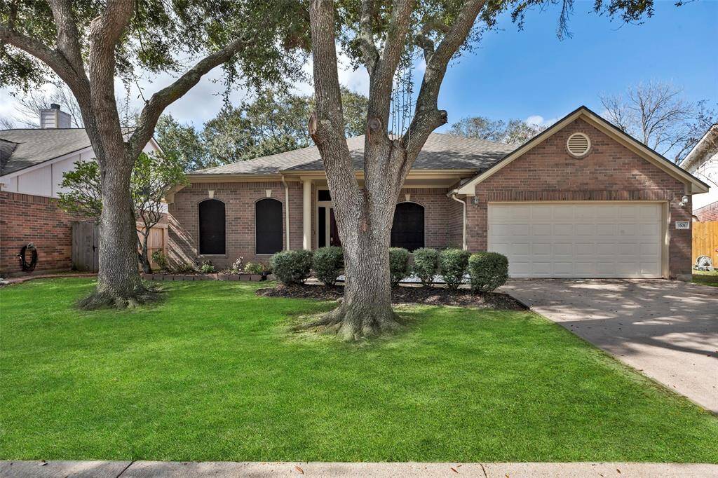 This charming brick home features a well-maintained front yard with mature trees and a two-car garage. The landscaping includes neat shrubbery, and the home has a welcoming entrance with arched windows, creating a cozy and inviting appearance.