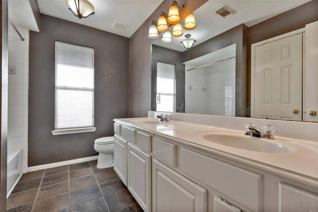 This bathroom features a modern design with a large mirror, double sink vanity, and sleek white cabinetry. The room is well-lit with stylish overhead lighting and includes a shower-tub combo and a window for natural light. The floor is tile, adding to the contemporary feel.