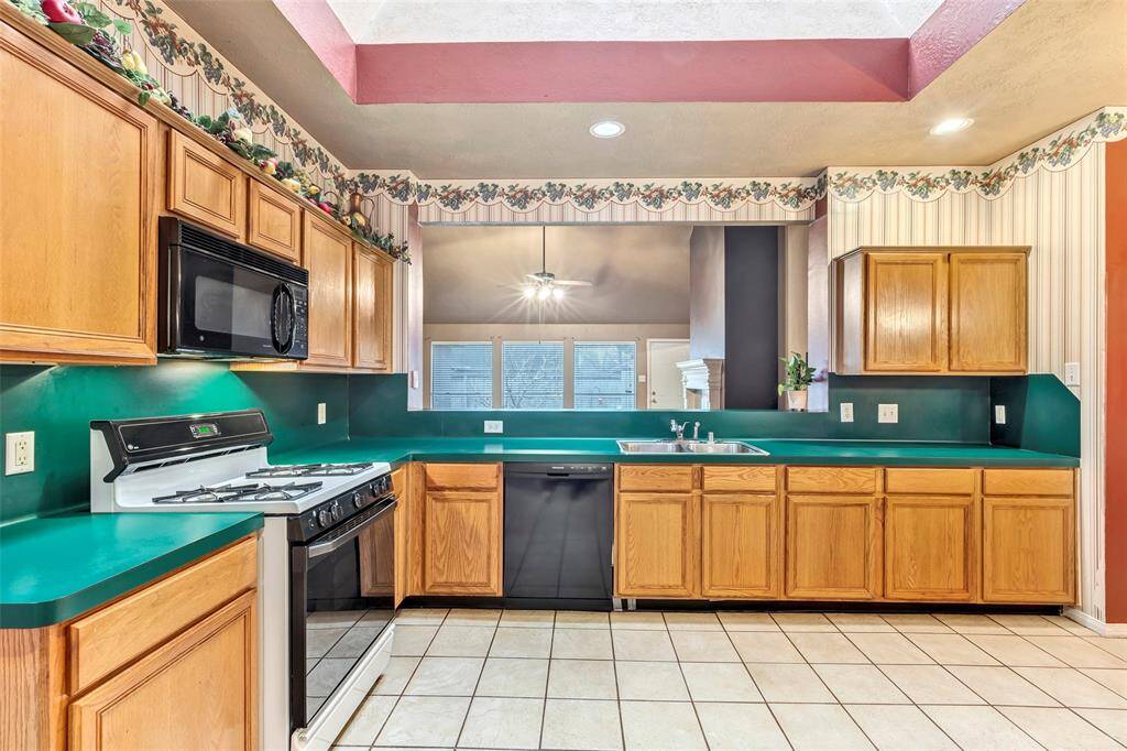 This kitchen features ample cabinetry, a dishwasher, gas stove,  and microwave. It opens up to a dining area with a view of a fireplace and large windows, offering a cozy, inviting space.