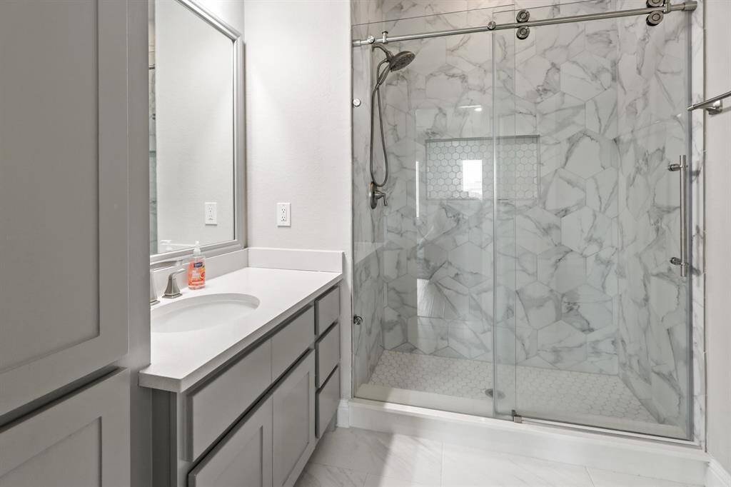 This en suite bathroom is situated off the large Secondary Bedroom and features glass encased shower with sliding door and custom tile surround as well as an extended vanity and additional storage space.