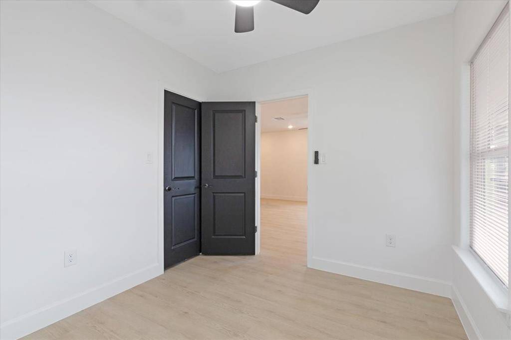This room features light wood flooring, white walls, and a ceiling fan. It has a window allowing natural light and a double-door entry, creating a bright and welcoming space. This could also be used as a home office.