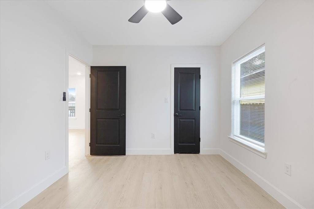 This bright room features light wood flooring, a large window for natural light, and two black doors adding a modern touch. It’s perfect for a bedroom or home office.