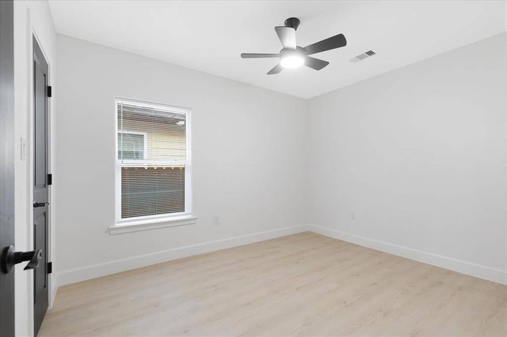 This room is bright and airy, featuring light wood flooring and neutral walls. It includes a window for natural light, a ceiling fan for comfort, and modern finishes, offering a versatile space for various uses.
