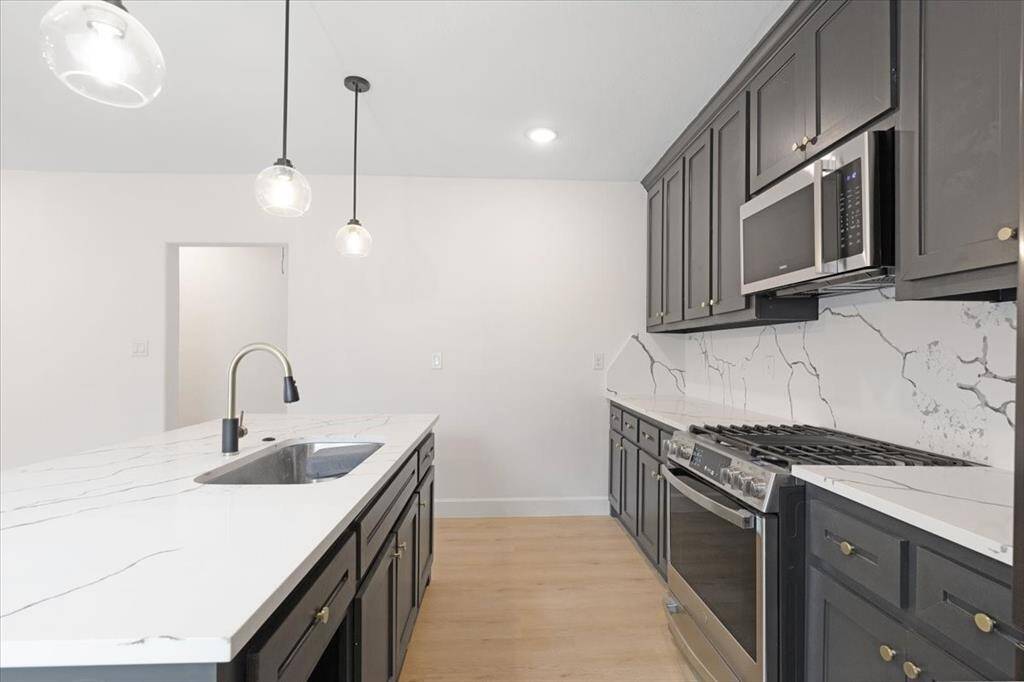 This modern kitchen features sleek dark cabinetry, stainless steel appliances, and a stylish marble-patterned backsplash. It includes a central island with a built-in sink and elegant pendant lighting, providing a functional and attractive space for cooking and entertaining.