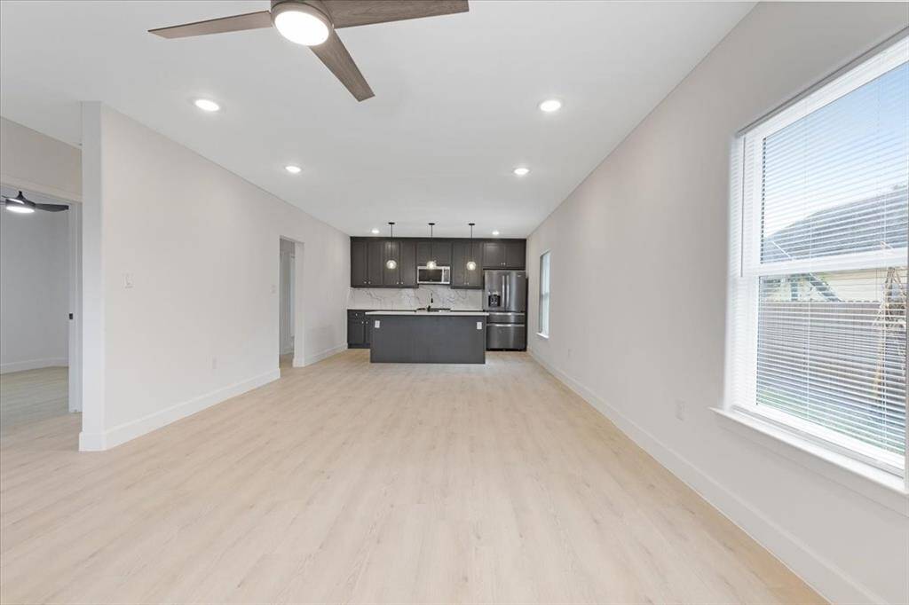 Bright, open-concept living space with modern kitchen, recessed lighting, and light wood flooring. Large windows provide plenty of natural light.