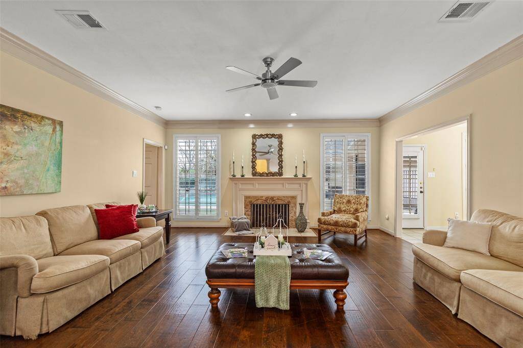 Spacious Family Room with Warm Wood Flooring, Neutral Walls, and Ample Natural Light. Features a Central Fireplace, Ceiling Fan, and Elegant Decor.