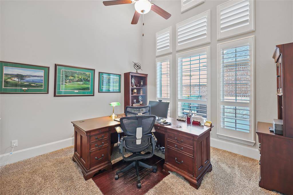 The study is enhanced with elegant plantation shutters. These timeless shutters allow natural light to filter through while providing beautiful views of the courtyard. The room is thoughtfully designed with neutral walls, plush carpeting, and tall baseboards, creating a sophisticated and welcoming space.