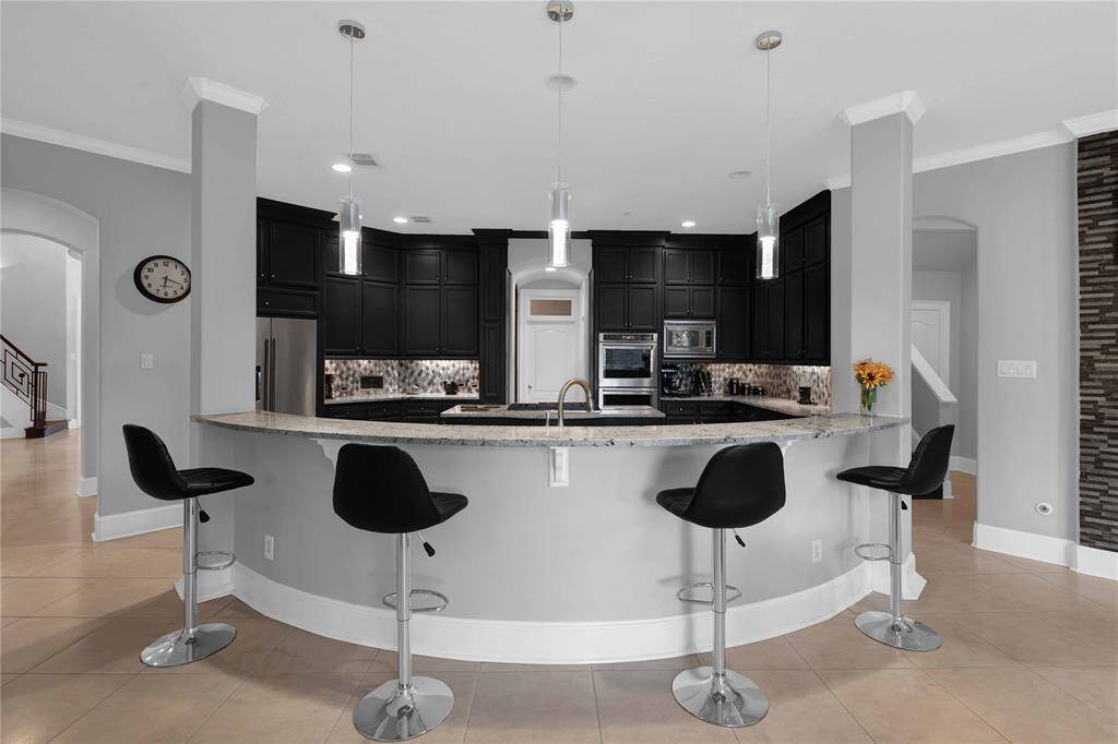 A large curved breakfast bar offers addiOonal seaOng, overlooking the kitchen and providing the perfect spot for relaxed meals or casual conversaOons. Elegant pendant lighOng hangs overhead illuminate the expansive space.