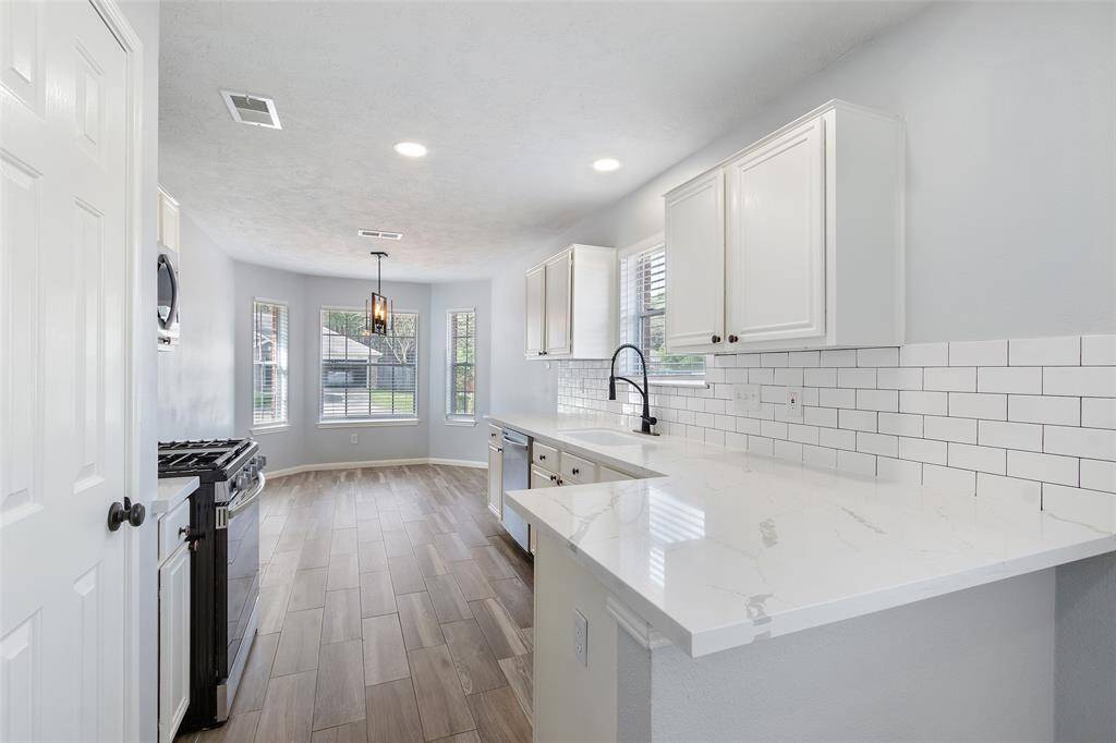 Bright and modern kitchen with white cabinetry, subway tile backsplash, and gorgeous Quartz countertops. The space features stainless steel appliances, a large window for natural light, and wood-look tile flooring.