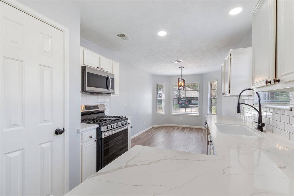 This kitchen features modern stainless steel appliances, white cabinetry, and a sleek Quartz countertop. It has a bright, open layout with a cozy dining nook and ample natural light from large windows.