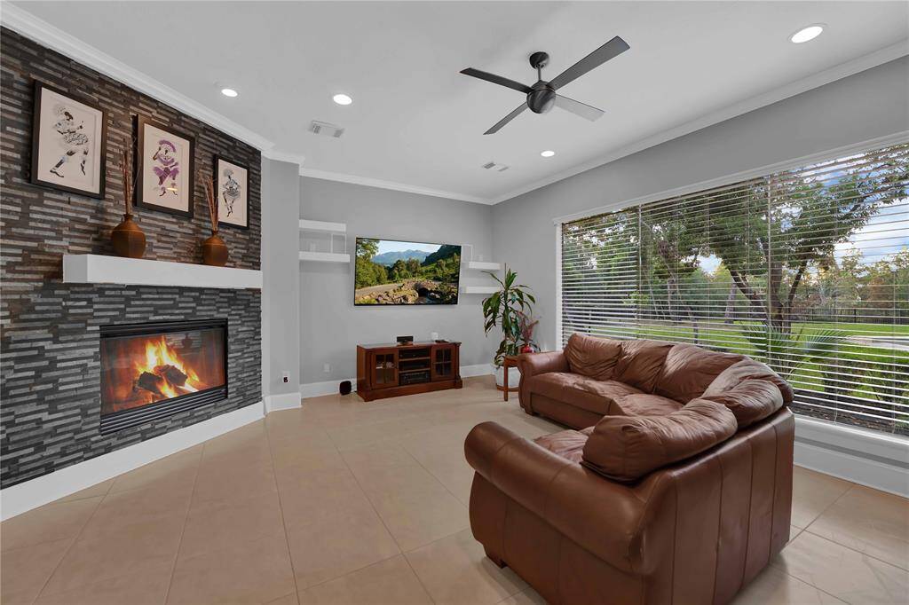 The living room is a capOvaOng centerpiece, featuring a large frameless window that offers unobstructed panoramic views of the beauOfully landscaped backyard, sparkling pool, and serene pond beyond. This design floods the space with natural light, fostering a warm and inviOng atmosphere.