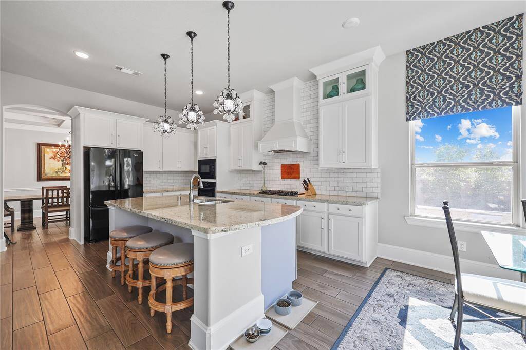 White cabinetry with elegant glass accents provides abundant storage, complemented by a timeless subway tile backsplash. Under the glow of stunning crystal-like pendant lights, this kitchen seamlessly combines luxury and practicality, making it a dream space for any home chef. The built-in oven, microwave and gas cooktop provide modern convenience, while the custom vent hood enhances both function and aesthetic appeal.