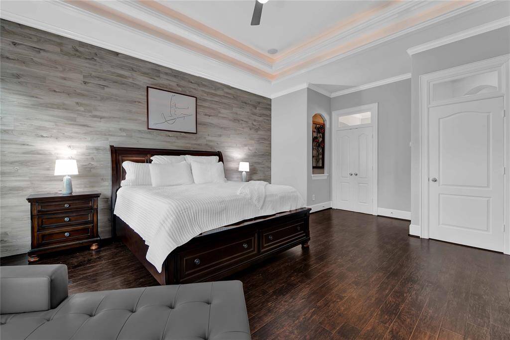 The primary retreat is elegantly adorned with soO paint, rich hardwood flooring, and a double tray ceiling with cove lighOng and crown molding. A beauOful accent wall and thick baseboards further enhance the room's sophisOcated and inviOng atmosphere, creaOng a warm and welcoming space.