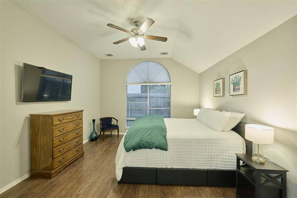 The spacious 1st floor primary suite features vaulted ceilings, a ceiling fan, huge window, and double doors leading to the primary bathroom.