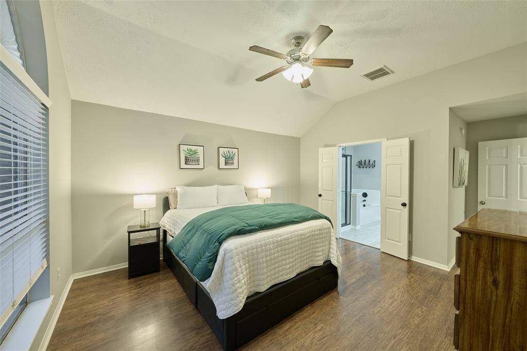 The spacious 1st floor primary suite features vaulted ceilings, a ceiling fan, huge window, and double doors leading to the primary bathroom.