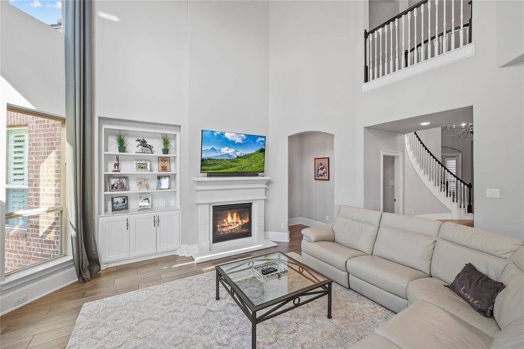 A striking stone fireplace creates the perfect focal point. To the left of the fireplace, a built-in shelving and cabinetry offers both display and storage space. The walls are painted in a soft neutral tone, complementing the flooring that runs seamlessly throughout the space.