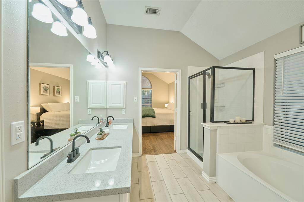 This updated primary bathroom features double sinks, a garden soaking tub, and black framed shower with neutral tile flooring.