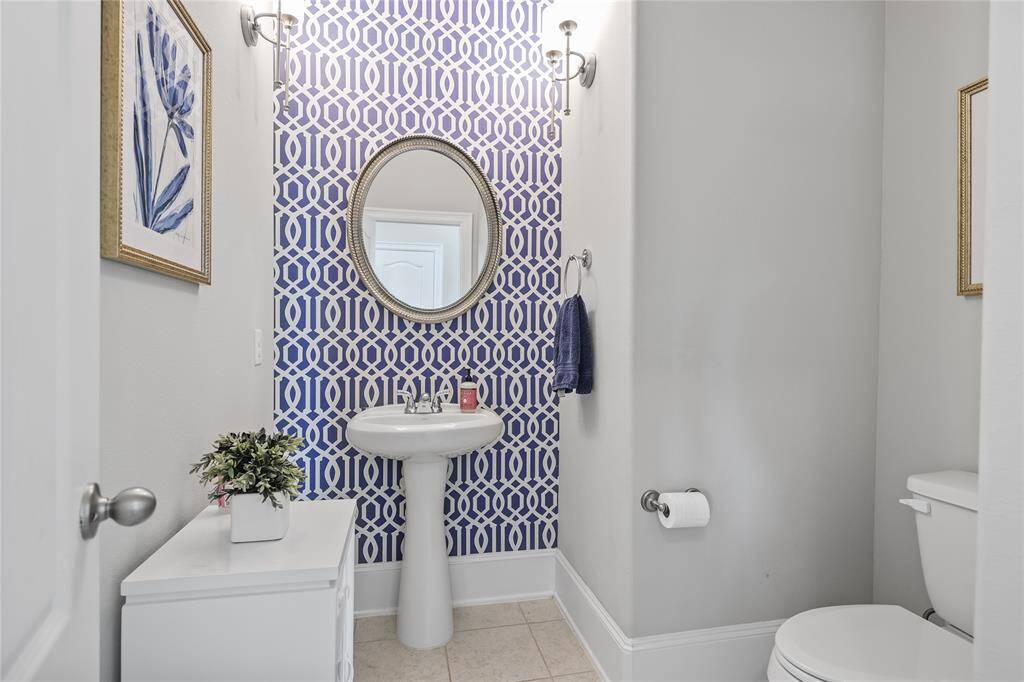 This stylish half bath features a bold geometric accent wall in blue and white, a pedestal sink with a framed round mirror above complemented by wall-mounted sconces for soft, ambient lighting.