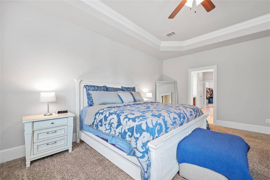 Access the primary ensuite bathroom effortlessly through the doorway. The tall baseboards and crown molding enhance the room's elegant design. The flooring consists of plush carpeting, adding warmth and comfort.