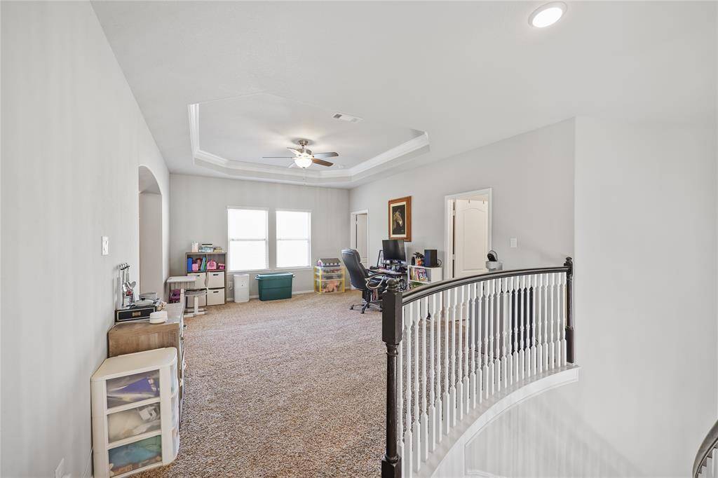 At the top of the stairway you are welcomed to the game room featuring a tray ceiling with crown molding and a ceiling fan with a light fixture. The neutral-toned carpeting adds warmth and comfort underfoot, making the room ideal for relaxation and entertainment.