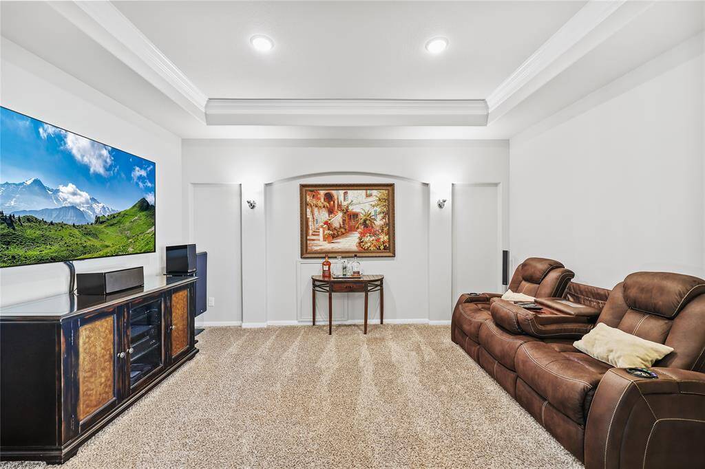 This media room offers a cozy and immersive entertainment experience, featuring a tray ceiling with crown molding. The walls are painted in a soft neutral tone, creating a comfortable atmosphere, while recessed lighting and wall sconces provide ambient illumination. The plush carpeting enhances sound absorption and comfort, making the space ideal for movie nights or gaming.