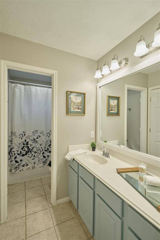 Secondary bathroom has long countertop with storage and a tub/shower combination.