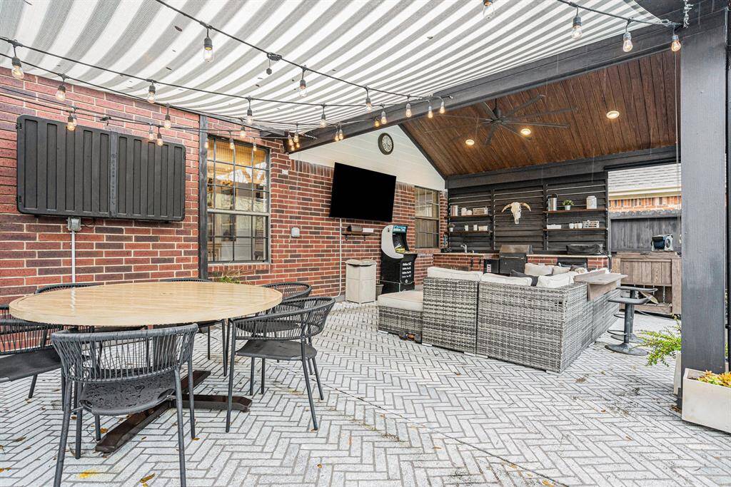 This outdoor space features a stylish covered patio with a cozy seating area, dining table, and TV.   Perfect for entertaining or relaxing.