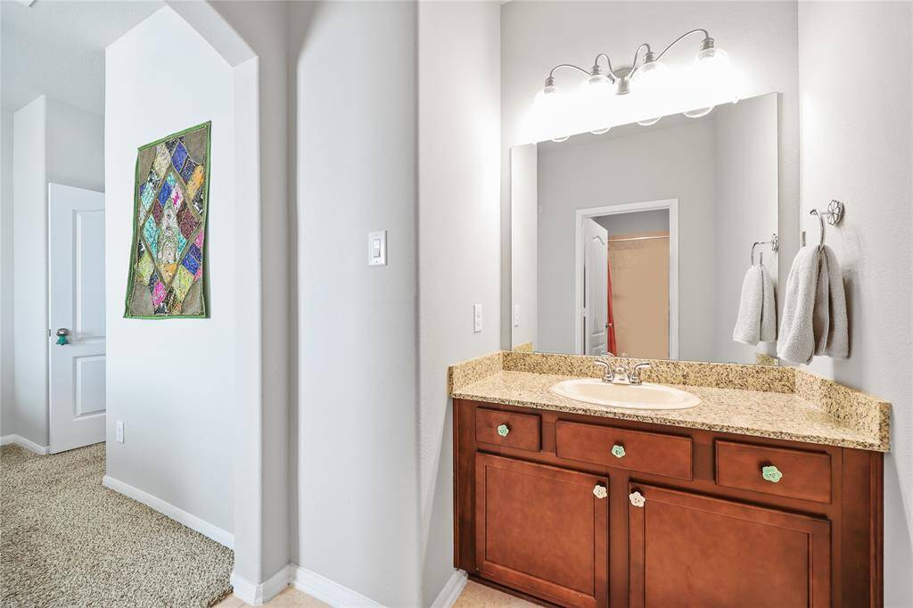 Vanity area to the secondary bedroom part of the Jack and Jill bathroom. The vanity features granite top with wooden drawer and cabinet area for storage.