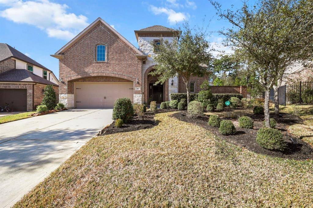 This spacious residence boasts a three-car, oversized garage with long, double wide driveway. The front yard is well-maintained with neatly trimmed bushes, trees, and a landscaped garden bed lined with decorative rocks. The elegant arched brick and stone entryway welcomes you to the home courtyard.