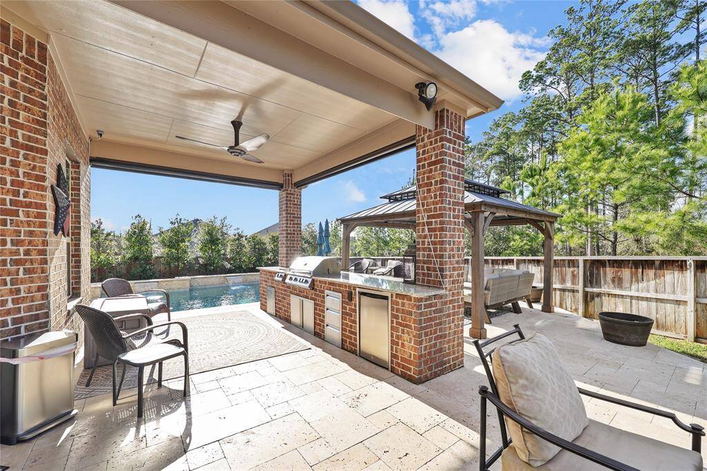 This outdoor kitchen and entertaining area offers a luxurious and functional space for outdoor dining and relaxation. The built-in kitchen features a stainless-steel grill, mini refrigerator, and storage cabinets, all set within a stylish brick and granite countertop design.