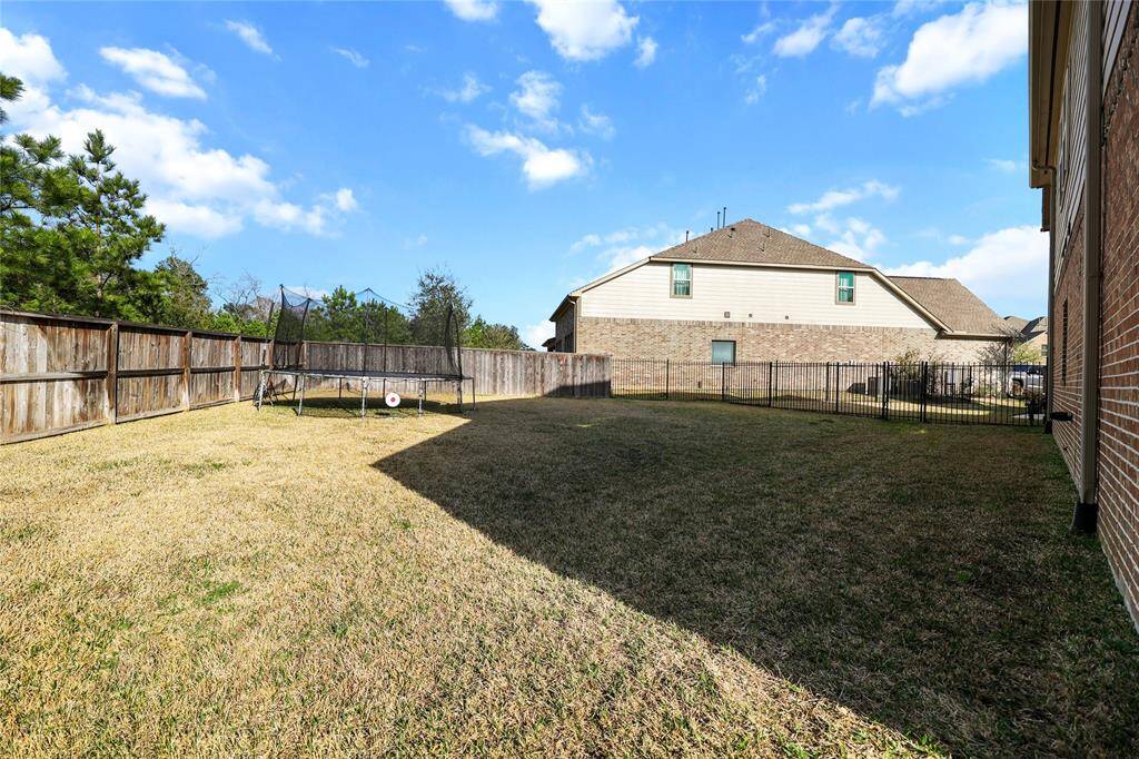 This spacious backyard offers a large open green space, perfect for recreation, gardening, or future outdoor enhancements. The yard is enclosed by a wooden privacy fence, providing seclusion while a black metal fence maintaining an open feel with views of the front courtyard.