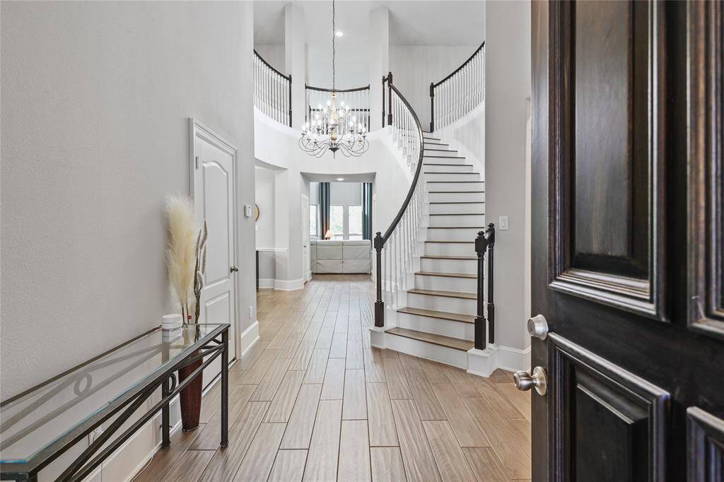 Step into a grand entrance featuring soaring ceilings, elegant wood-look tile flooring, and a breathtaking cascading staircase with stylish black handrails and white wooden spindles. A gorgeous chandelier adds a touch of sophistication, illuminating the bright and airy space.