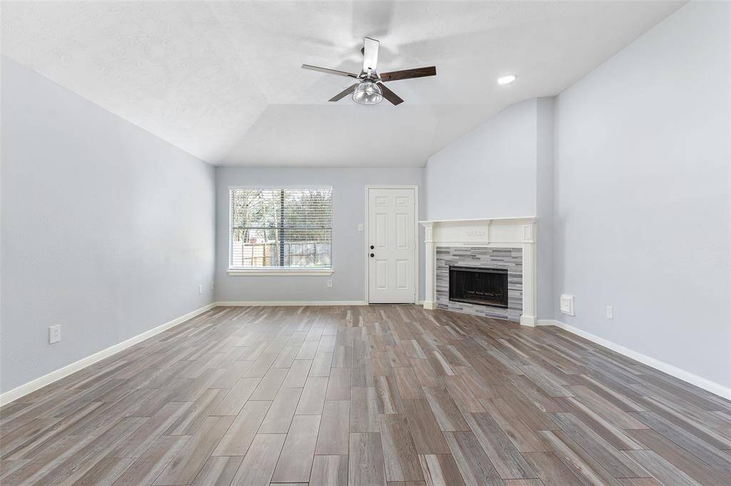 This spacious living room features a vaulted ceiling, modern ceiling fan, and a fireplace with a sleek tile surround. The room is bright, with large windows offering natural light.