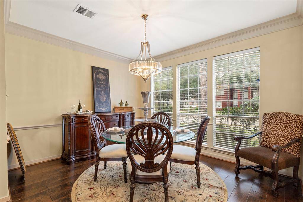 This Dining Area Features a Classic, Elegant Design with a Glass-Top Table and Ornate Wooden Chairs. Large Windows Provide Ample Natural Light, while a Stylish Chandelier adds a Touch of Sophistication. The Room is accented by a Decorative Sideboard and Neutral Walls, Creating a Warm and Inviting Atmosphere.