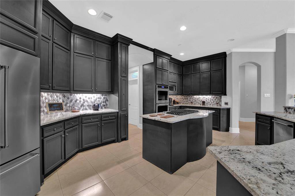 The oversized kitchen is quipped with stainless steel appliances including double ovens, a gas cooktop, dishwasher, and a built-in fridge. Gleaming granite countertops and dark cabinetry combine with high ceilings and recessed lighOng to enhance the elegance and grandeur of this impressive kitchen.