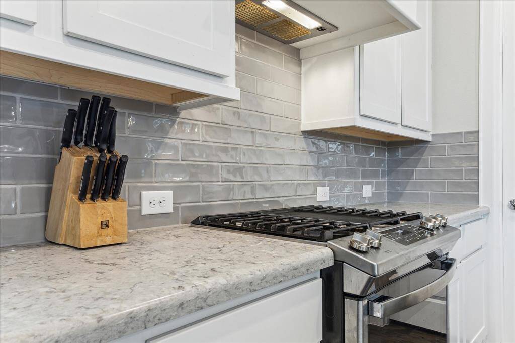 The camera zooms in on the subway tile backsplash, offering a detailed view of its design. Next, it focuses closely on the stainless steel stove, highlighting its suitability for a chef.