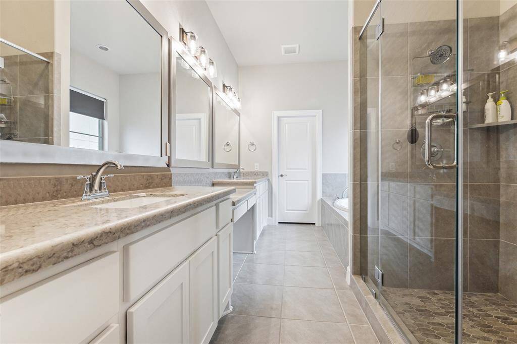 Welcome to the primary bathroom, which features two sinks, tile flooring, and both a walk-in shower and a soaking tub. This space offers the perfect blend of functionality and relaxation, making it ideal for your daily routines and unwinding after a long day. With its thoughtful design and modern amenities, this bathroom provides everything you need for comfort and convenience.