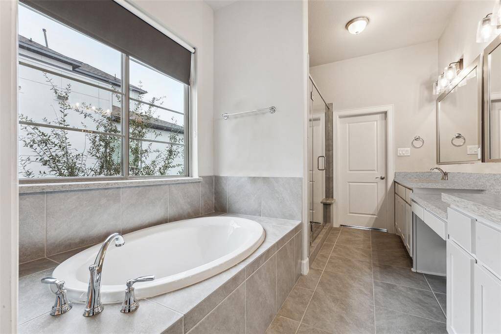 This bathroom view reveals an expansive bathtub, with an abundance of natural light streaming in through the windows. The large tub is the centerpiece of the room, inviting relaxation and providing a serene atmosphere. The ample windows allow sunlight to flood the space, enhancing the tranquil ambiance and highlighting the elegant design of the bathroom.