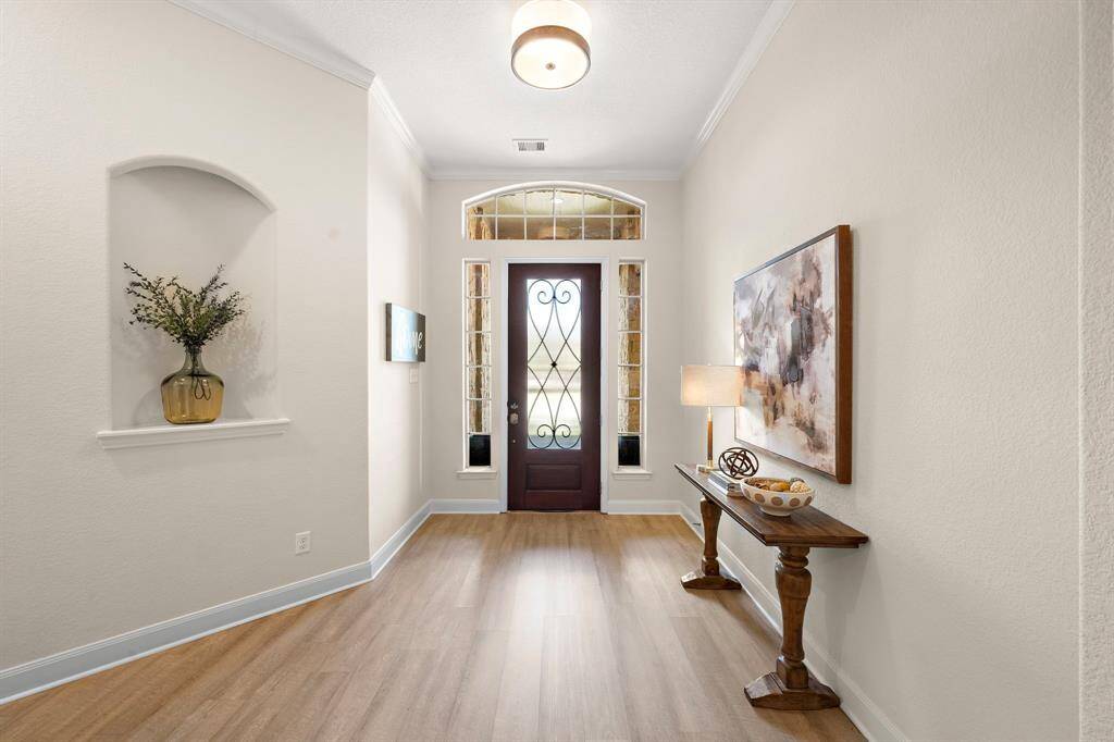 Elegant entryway showcasing a covered archway and decorative shelving, setting the tone for stylish living. The warm wood-inspired flooring leads guests seamlessly into the entertainment areas, enhancing the inviting atmosphere of this Spring Trails home.