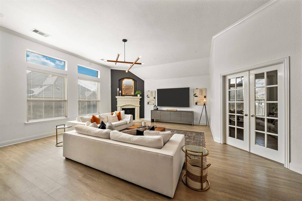 Explore a light-filled living room with expansive windows that illuminate the space. Featuring designer lighting fixtures, a cozy fireplace, and patio access, this room’s layout invites both entertaining and relaxation. The open design seamlessly integrates a home office area, blending functionality with style.