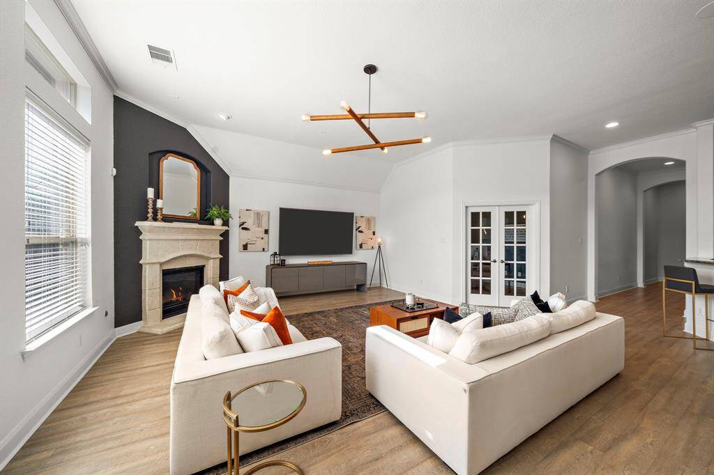 Effortlessly combining comfort and style, the living room features expansive windows and designer lighting fixtures. A cozy fireplace enhances warmth, while the open layout offers seamless access to a home office and patio, making it ideal for gatherings or serene retreats.