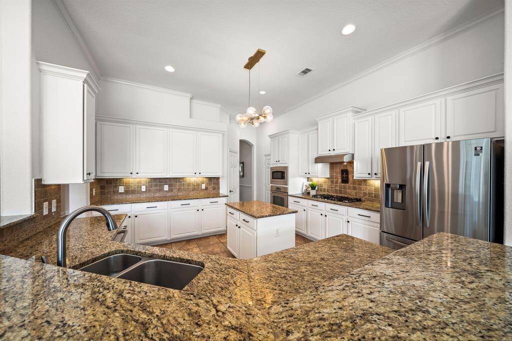 The kitchen features elegant white cabinetry and granite countertops, providing ample storage and workspace. Stainless steel appliances and a central island enhance its functionality, while a breakfast bar offers casual seating, creating an inviting setting for culinary creativity and gatherings.