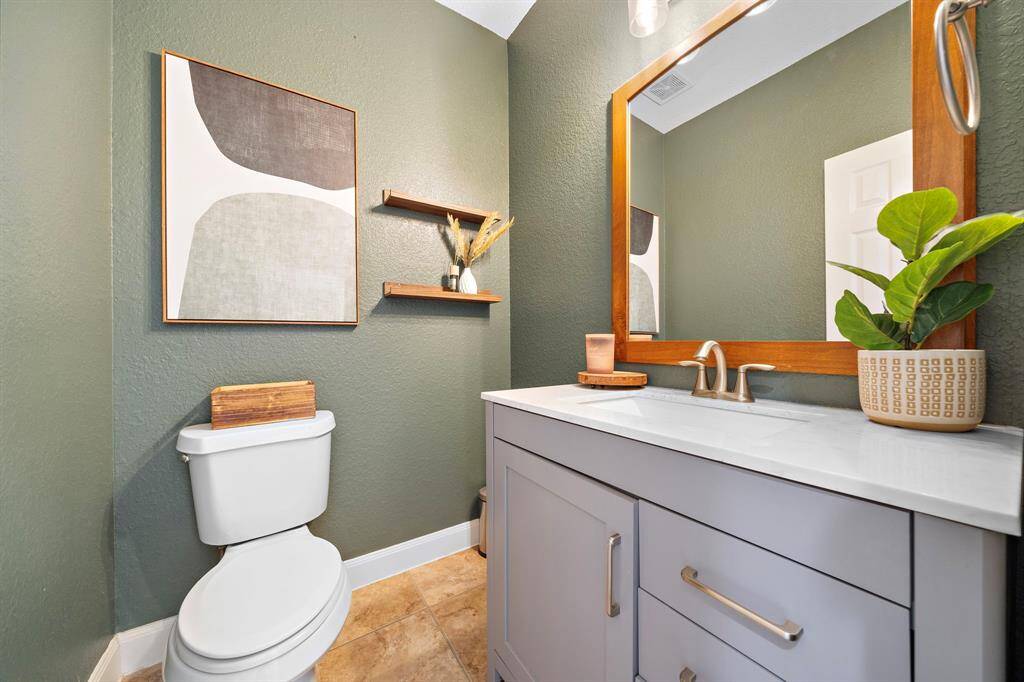 This elegantly appointed half bath features an exquisite vanity and contemporary fixtures. Thoughtful design elements like open shelving and stylish wall decor enhance the space, creating a refined yet welcoming atmosphere that blends functionality with aesthetic appeal seamlessly.