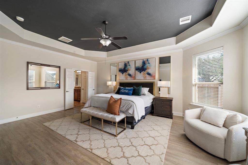 This elegant primary bedroom features a tray ceiling and refined details, showcasing an ideal retreat within the home. Abundant natural light fills the room, enhancing its spacious feel and comfortable ambiance.