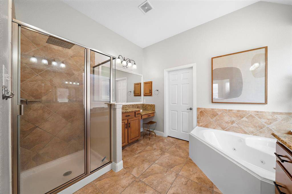 The primary bath features dual vanities, a soaking tub, and a glass-enclosed shower, offering both luxury and functionality. Tile flooring and elegant finishes create a serene environment for relaxation.