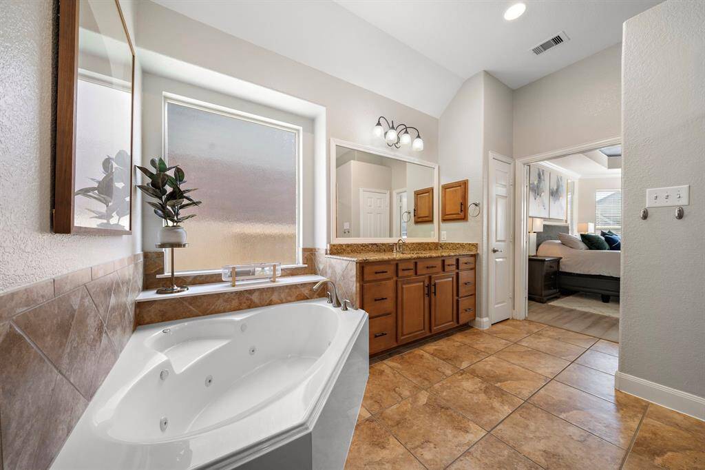 Indulge in the spa-like serenity of the primary bath, complete with a luxurious soaking tub and dual vanities featuring granite countertops. The glass-enclosed shower enhances the space's elegance, while warm tile flooring and natural light create an inviting atmosphere for relaxation and rejuvenation.