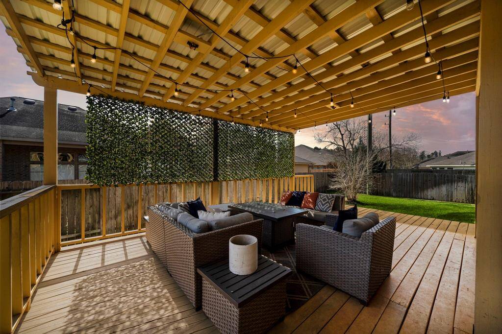 Covered patio with a pergola features a spacious seating area ideal for outdoor entertaining. Enjoy the wood decking and lush green space, creating an inviting extension of the home's living areas.