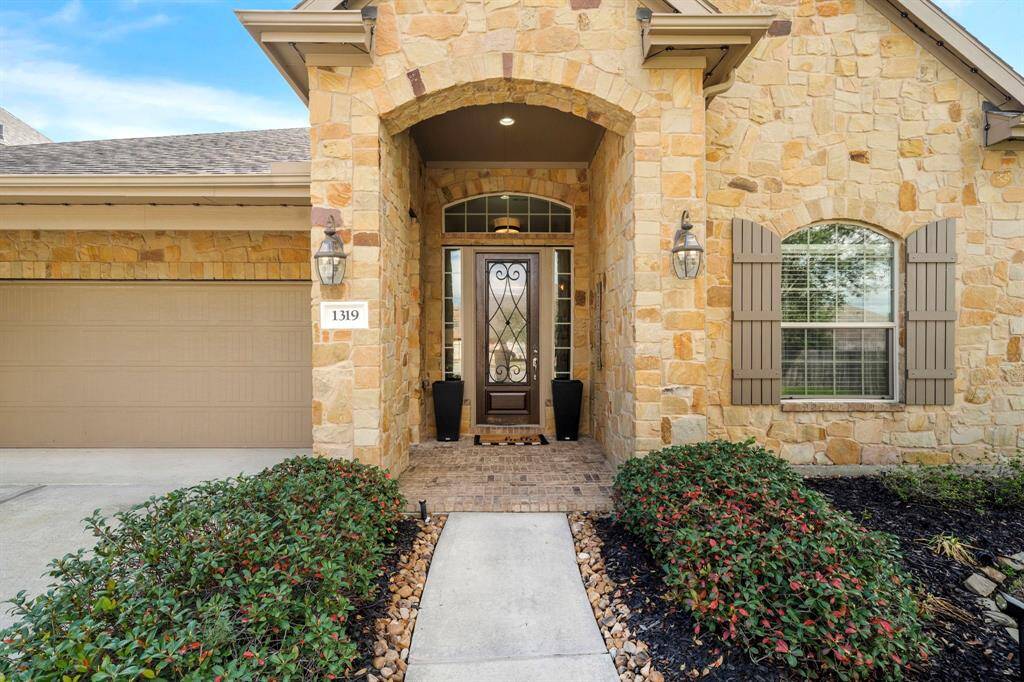 The covered entry features a stone archway, with decorative sconces adding a touch of elegance. A tandem garage completes the exterior.