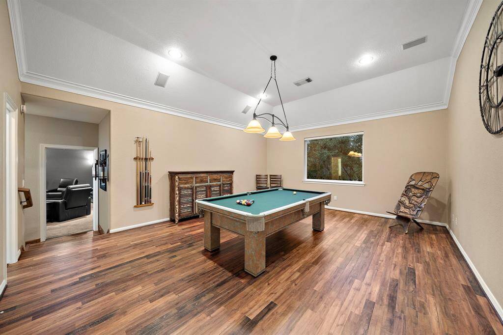 Entertainment takes center stage in this generously sized game room, where vaulted ceilings and recessed lighting create an airy, inviting ambiance. Warm hardwood floors add a touch of sophistication, while a large window brings in soft natural light. Whether for recreation or relaxation, the flexible layout offers endless possibilities for enjoyment.