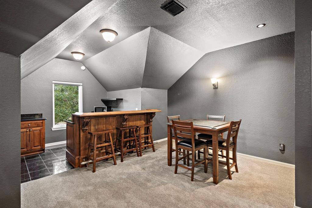 Upstairs secondary living area with a custom bar, offer casual seating and storage space. Newer carpet and unique ceiling fixtures enhance the space, offering an escape for relaxation and entertainment.